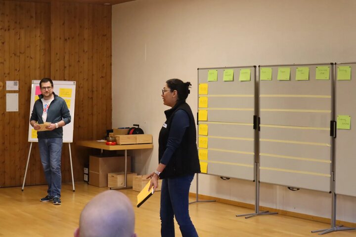 Two participants facilitating the session marketplace in front of a board of sticky notes